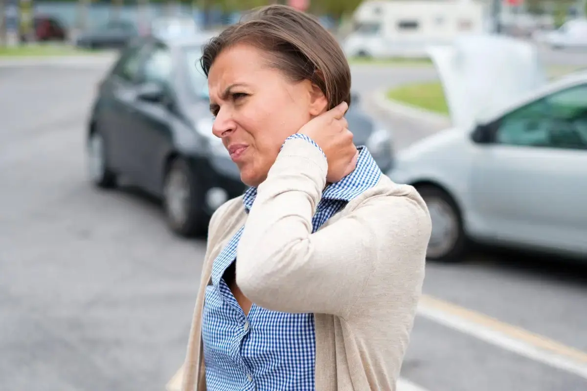 Woman grimacing and holding her neck beside cars on a road