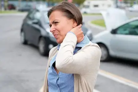 Woman grimacing and holding her neck beside cars on a road